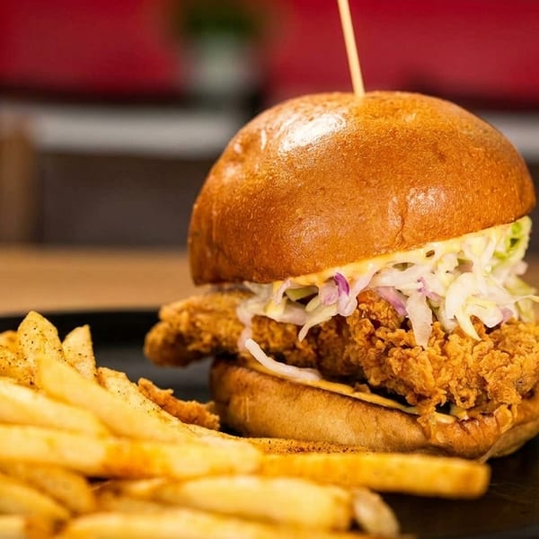 Crispy fried chicken sandwich with coleslaw and a side of seasoned french fries on a black plate.